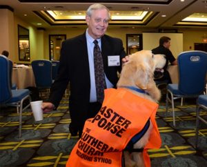 The Rev. Glenn Merritt, director of LCMS Disaster Response, greets a Golden Retriever with the Lutheran Church Charities K-9 Comfort Dog Ministry at the 5th LCMS National Disaster Response Conference in St. Louis. During breaks at the Oct. 7-10 event, pastors knelt to pet and pose for pictures with the cuddly canines. (LCMS Communications/Amanda Booth)