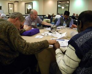 The Rev. Jacob Gillard of the World Mission Prayer League, second from left, leads a prayer during a table discussion at this year's conference of the Association of Lutheran Mission Agencies. (LCMS Communications/Paula Schlueter Ross)