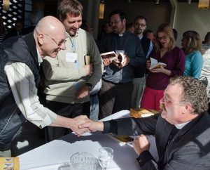 While signing his book Christ have Mercy: How to Put Your Faith in Action at the LCMS International Disaster Conference, Synod President Rev. Dr. Matthew C. Harrison, seated, greets the Rev. _______ Mikulas of Argentina. (LCMS/Pamela J. Nielsen)