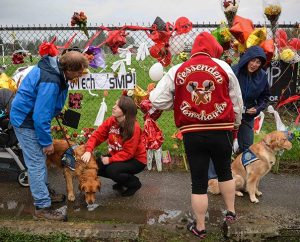 Lutheran Church Charities "comfort dog" handlers Tom Bartnik, with Luther, and Jeanne Moore, with Aaron, visit the memorial along the fence of the Marysville-Pilchuck (Wash.) High School. (Ron Norris)