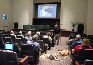 Tim Hetzner, president of Lutheran Church Charities, leads a presentation on using "K-9 Comfort Dogs" in disaster response. Hetzner described the golden retrievers as "lovers" by nature who are "great listeners and nonjudgmental." The photo on the screen behind him shows a young man lying on a floor with comfort dog "Howie." The young man — who was grieving his girlfriend, who died in a car accident — stayed with the dog for 45 minutes, Hetzner said. (LCMS/Paula Schlueter Ross)