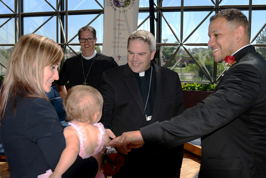 The Rev. Micah Glenn, right, gets the attention of his daughter, Talitha, and wife, Dorothy, after the June 17 Service of Sending for Glenn and the Rev. Antonio Lopez, the Synod's newest national missionaries. The couple also has a son, Jonathan, and are expecting a third child. Also pictured, from left, are the Rev. Steven Schave, director of Church Planting and Urban & Inner-City Mission with the LCMS Office of National Mission, and LCMS Missouri District President Rev. Dr. Lee Hagan. (LCMS/Al Dowbnia)