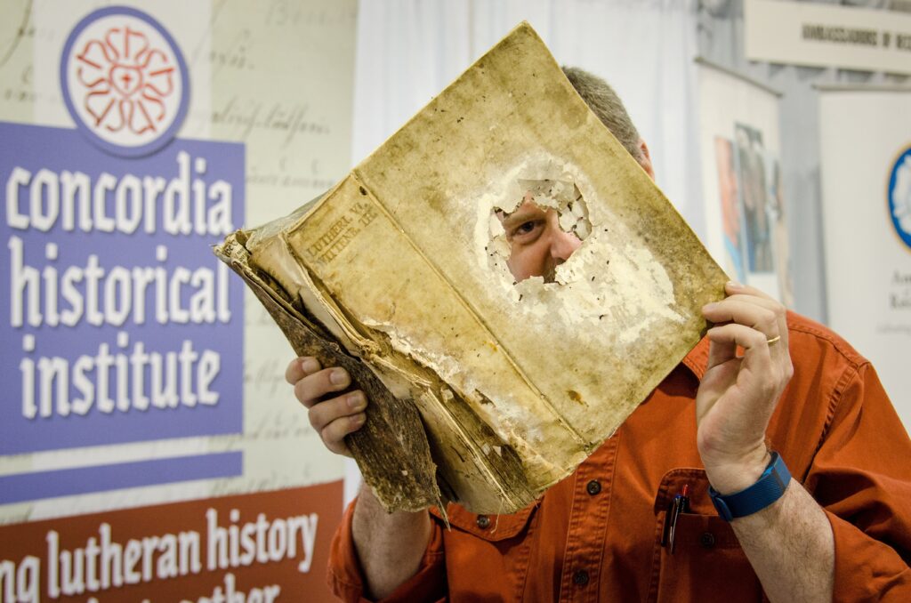 The Rev. Dr. Daniel Harmelink, executive director of Concordia Historical Institute, exhibits an original copy of Luther's Works Volume VI published in 1553 in Wittenberg, Germany, on Friday, July 8, 2016, before the start of the 66th Regular Convention of The Lutheran Church–Missouri Synod at the Wisconsin Center in Milwaukee. (LCMS/Frank Kohn)