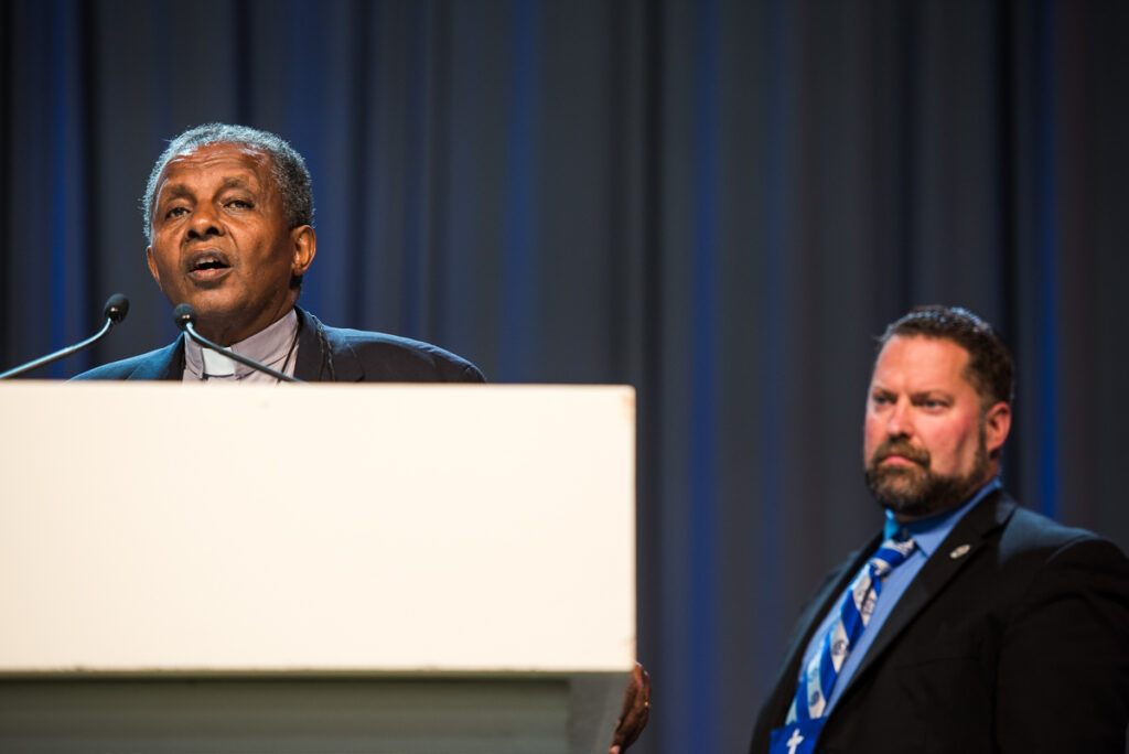 The Rev. Dr. Berhanu Ofgaa, general secretary of the Ethiopian Evangelical Church Mekane Yesus, thanks God for and encourages the two LCMS seminaries on Wednesday, July 13, 2016, at the LCMS convention in Milwaukee. The Rev. Dr. Albert B. Collver III, assistant to the LCMS president and director of church relations, introduced Ofgaa. (LCMS/Michael Schuermann)