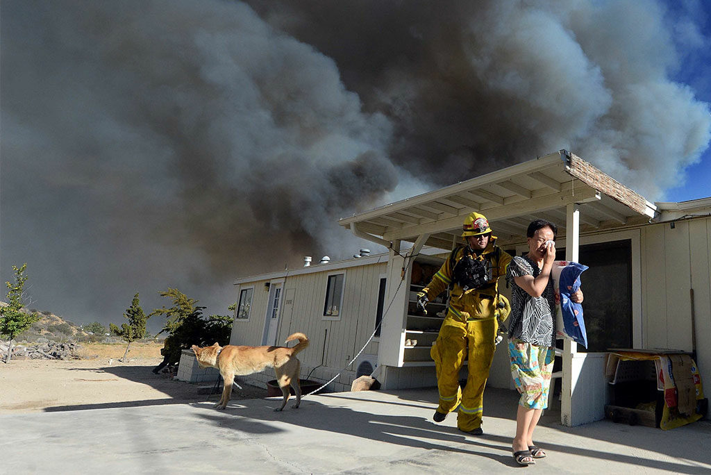 Firefighter Jeremy Pendergraft helps a woman out of her home as a wildfire off of Hwy. 138 approaches Aug. 16 in San Bernardino, Calif. (Will Lester/The Inland Valley Daily Bulletin via AP)