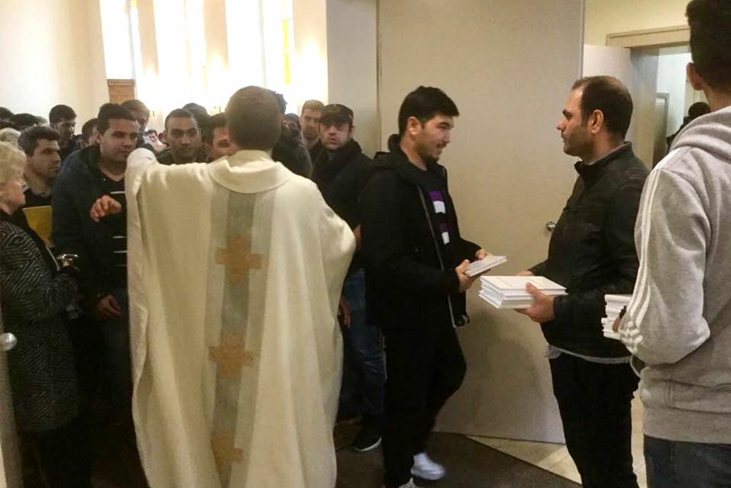 Copies of the new Luther’s Small Catechism in Farsi are distributed as the Rev. Gottfreid Martens (in the clerical vestment) greets parishioners at Trinity Evangelical Lutheran Church in Berlin. (Lutheran Heritage Foundation)
