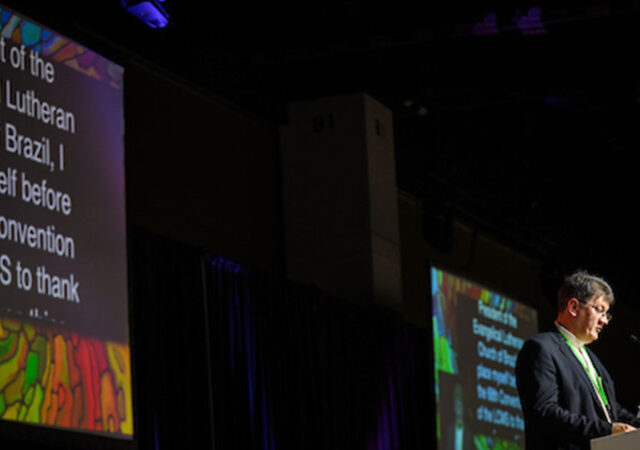 The Rev. Geraldo Walmir Schüler, president of the Evangelical Lutheran Church of Brazil, addresses the 68th Regular Convention of The Lutheran Church—Missouri Synod in Portuguese on July 30, 2023. A translation of his speech appears on the screen behind him. (LCMS/Erik M. Lunsford)