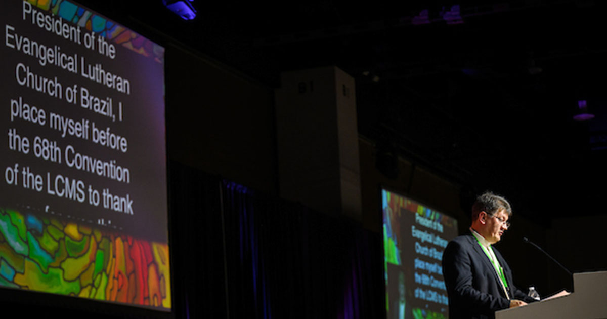 The Rev. Geraldo Walmir Schüler, president of the Evangelical Lutheran Church of Brazil, addresses the 68th Regular Convention of The Lutheran Church—Missouri Synod in Portuguese on July 30, 2023. A translation of his speech appears on the screen behind him. (LCMS/Erik M. Lunsford)