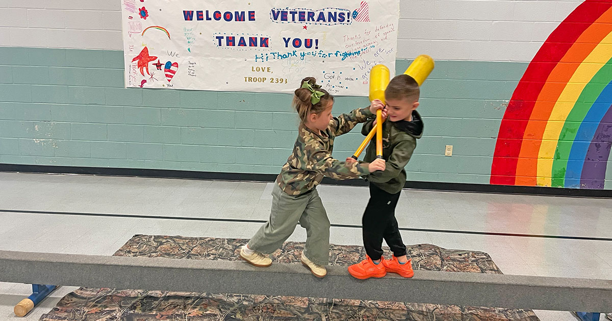 Students at Holy Trinity Lutheran School (HTLS) in Bowling Green, Ky., participate in a “boot camp” obstacle course, “jousting” on a balance beam while trying to avoid falling into the “mud pit,” during a Veterans Day celebration at the school on Nov. 11, 2025. (HTLS) 