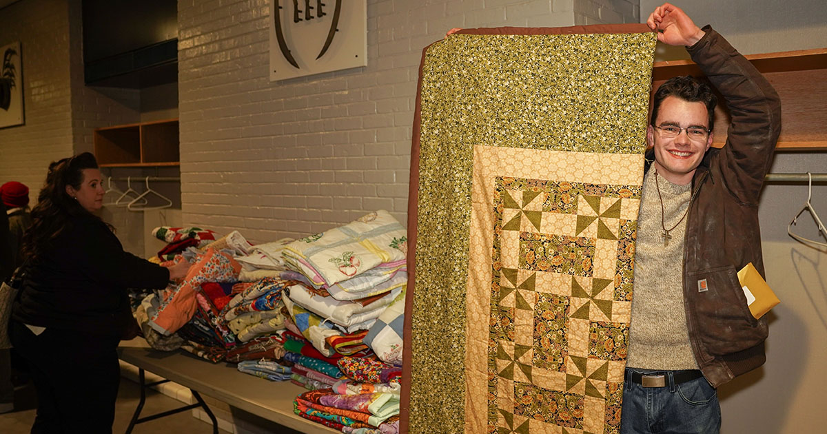 Elijah Anderson, a first-year student at Concordia Theological Seminary, Fort Wayne (CTSFW), poses with a quilt donated by supporters of the seminary. (CTSFW)