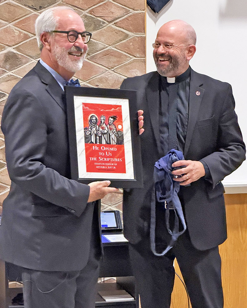 The Rev. Dr. Arthur A. Just Jr. holds up a framed facsimile of his surprise festschrift before he was to make a presentation at Concordia Theological Seminary, Fort Wayne (CTSFW). Also pictured is the Rev. Dr. Jon Bruss, CTSFW president. (Andrew Pohlod)