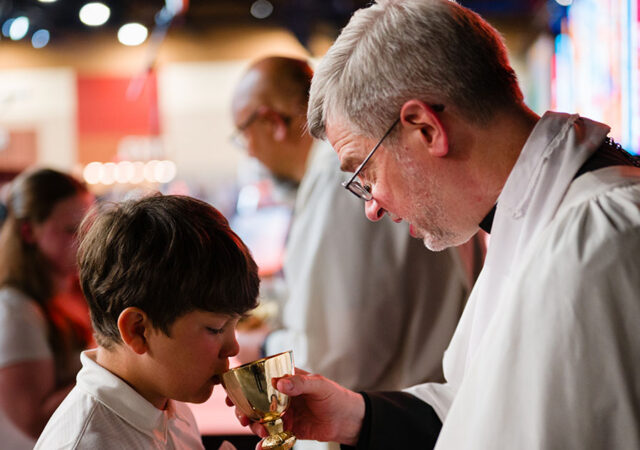 Choir member Lachlan Lee receives Holy Communion from the Rev. Dr. D. Richard Stuckwisch, president of the LCMS Indiana District, during the convention’s Opening Divine Service. (LCMS/Roy S. Askins)