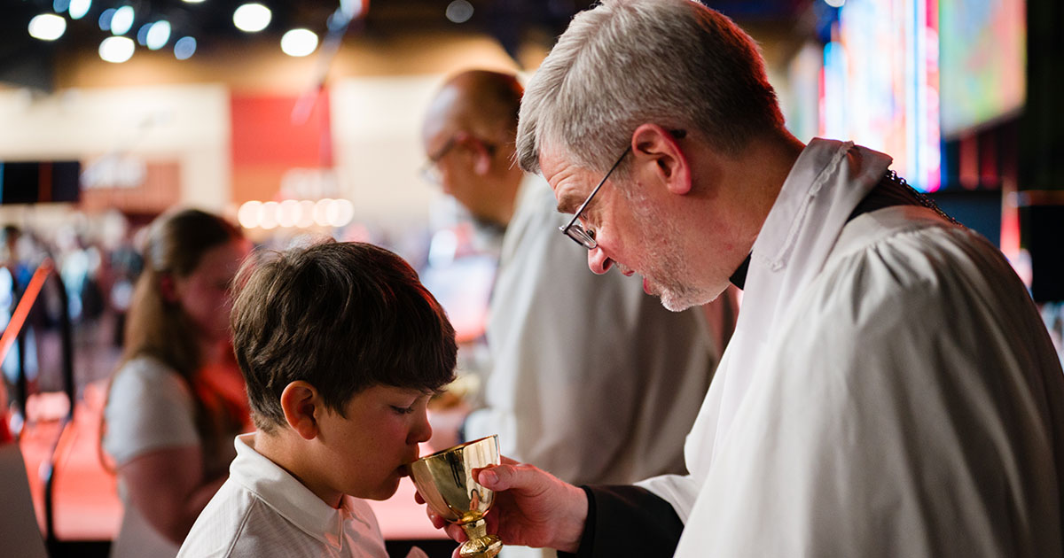 Choir member Lachlan Lee receives Holy Communion from the Rev. Dr. D. Richard Stuckwisch, president of the LCMS Indiana District, during the convention’s Opening Divine Service. (LCMS/Roy S. Askins)